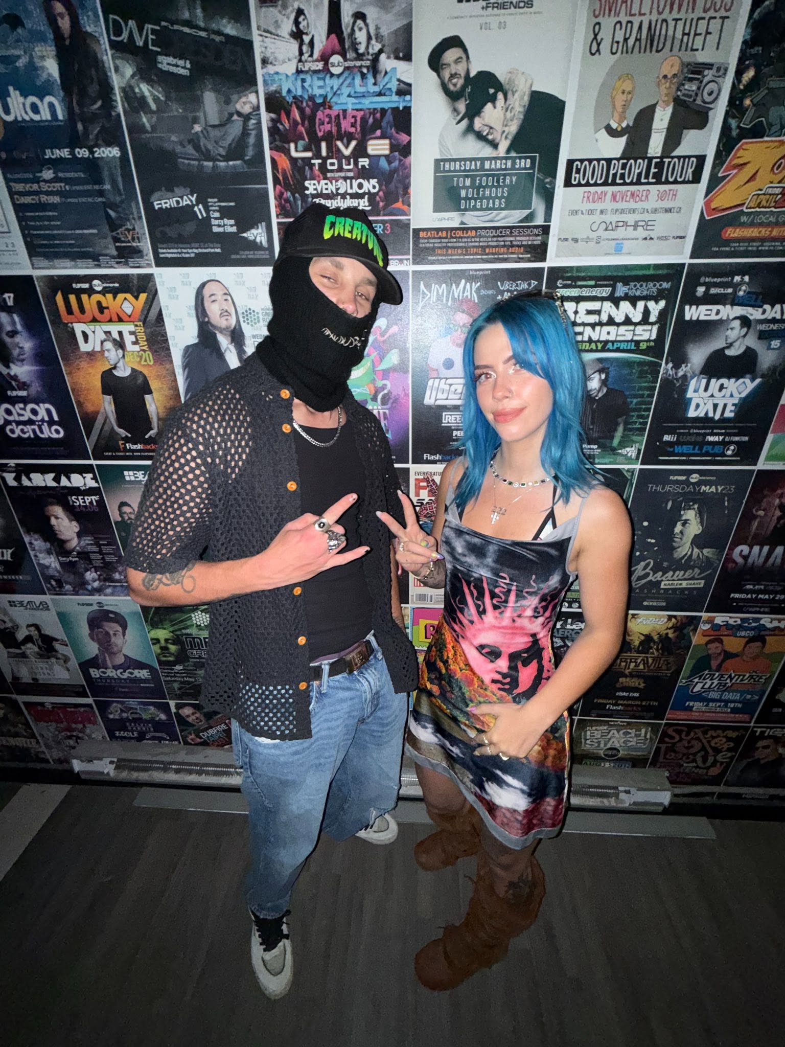 ROZENZA posing with a friend in front of a wall of concert posters